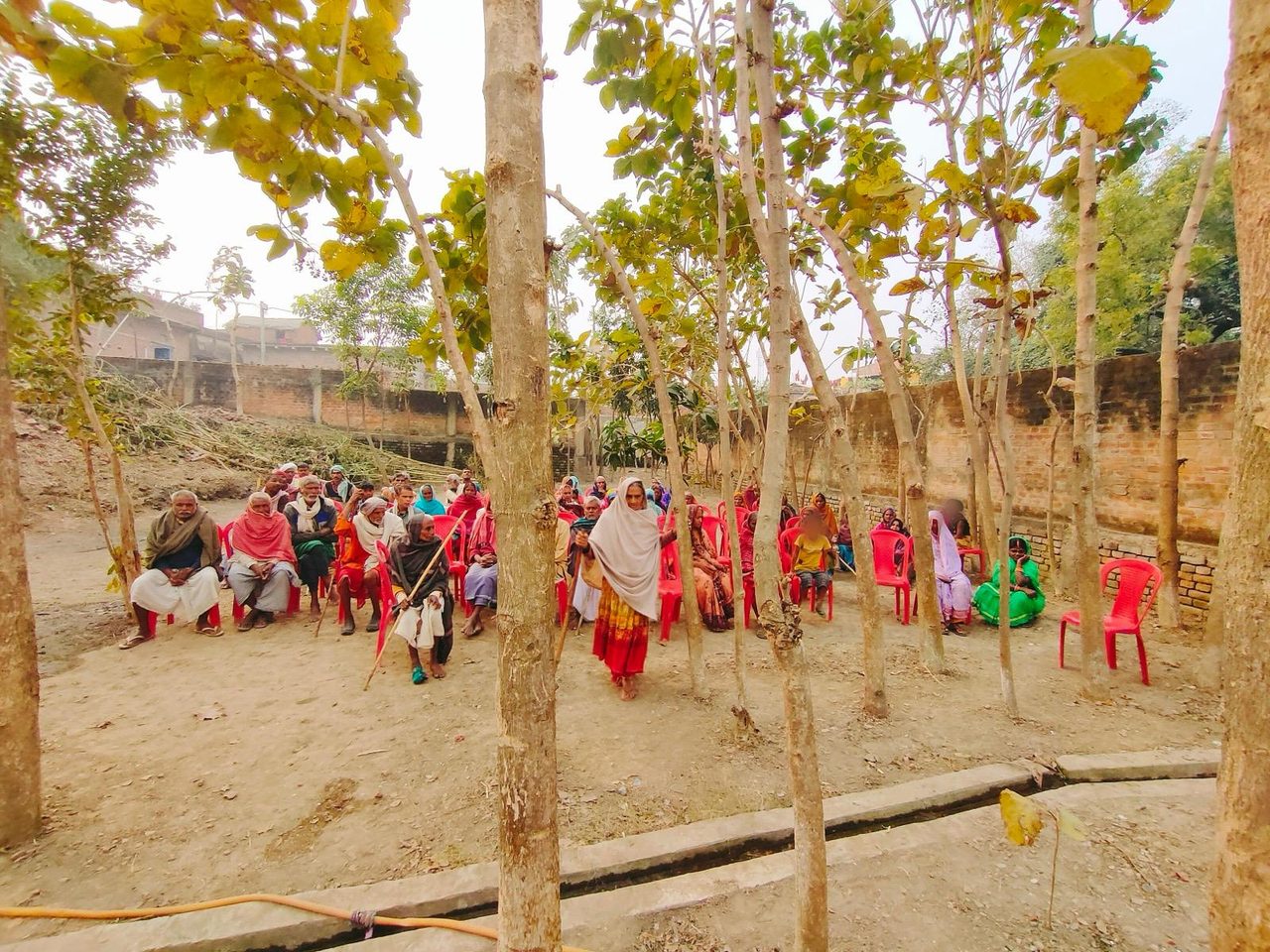 Villagers gathered on chairs in a tree-shaded courtyard at the December 2021 clothing distribution.